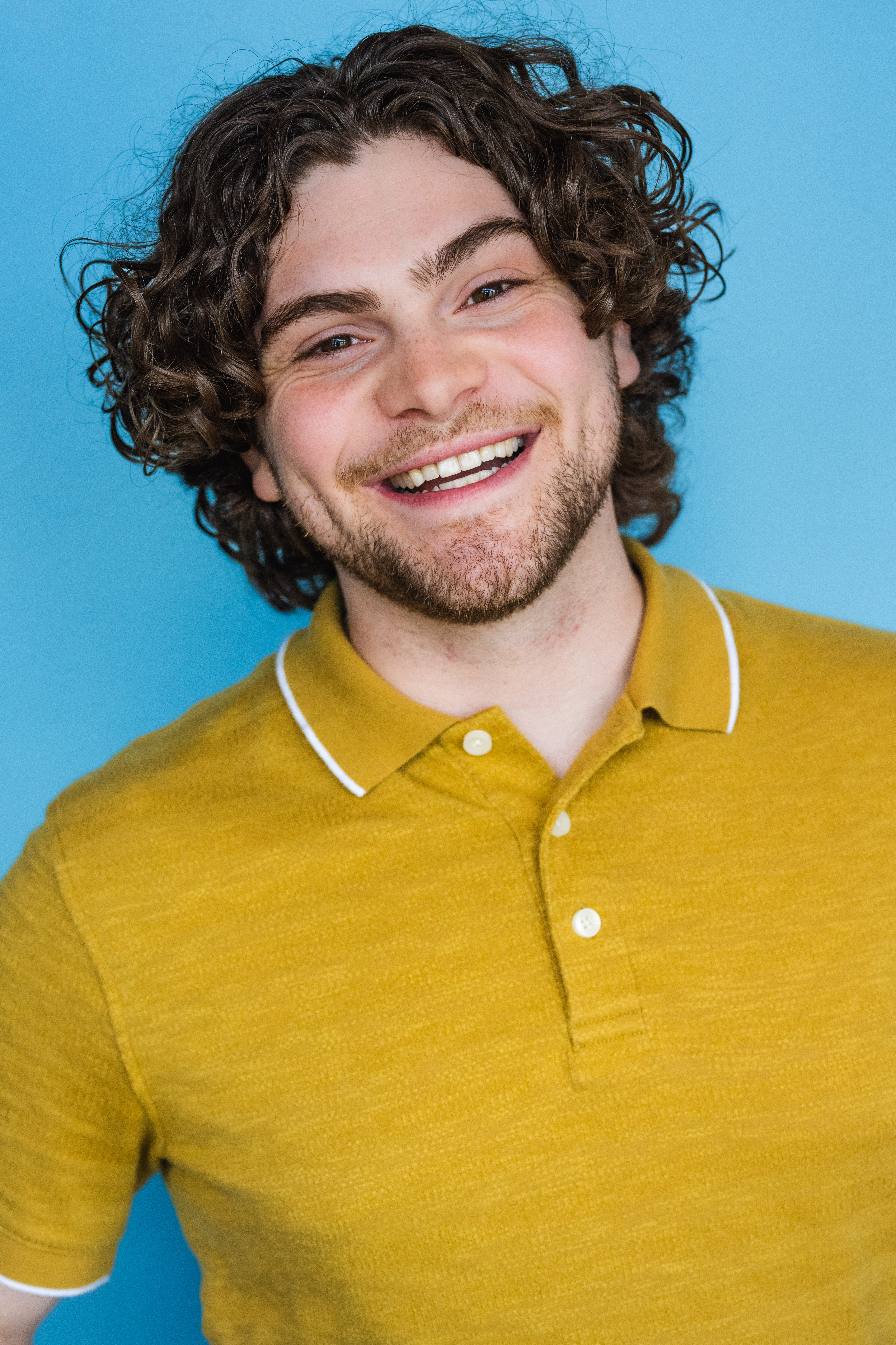 Garrett Stephenson smiling in a mustard polo against a blue background